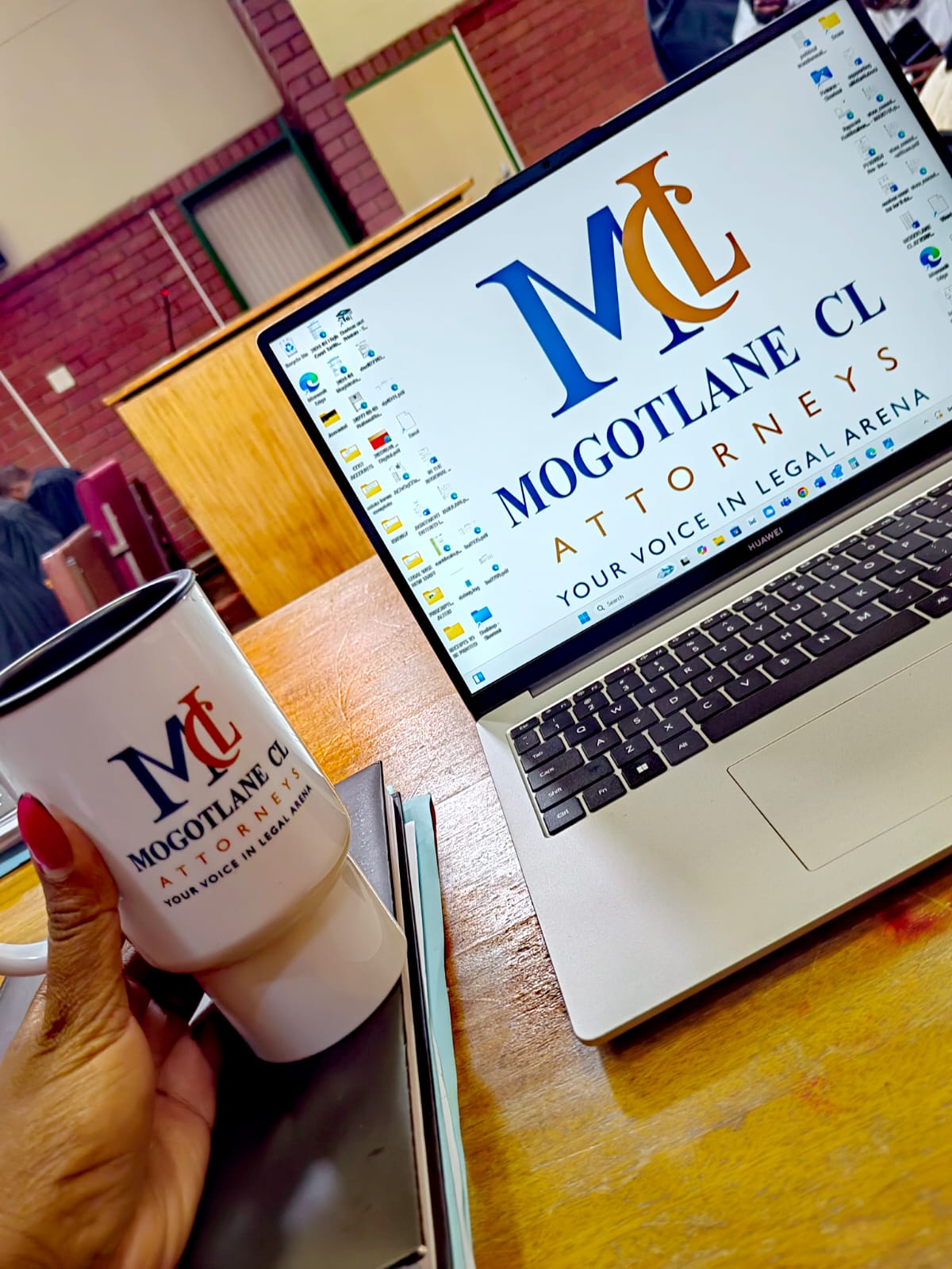 A desk in the courtroom with a laptop and an MCL branded mug, robed colleagues in the background